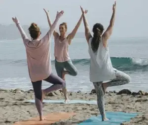 Three people practicing yoga on the beach at sunset, using gentle movement as a coping skill for hyperarousal.