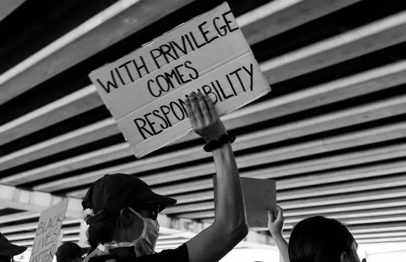 Image shows a man holding a sign stating "With privilege comes responsibility," reflecting on the challenges of being a white ally