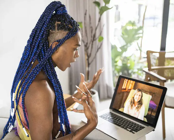 Non-binary individual participates in virtual EMDR therapy session, engaging with the therapist through a laptop screen.