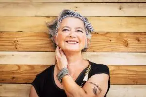 Cheerful woman with a tattooed arm smiling against a wooden background, representing healing and reflecting on how much is EMDR therapy?