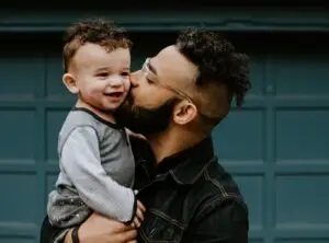 A young black man gently kisses the cheek of a black child, symbolizing a healthy parent-child relationship after know how to heal from childhood abuse.