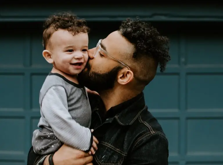 A young black man gently kisses the cheek of a black child, symbolizing a healthy parent-child relationship after know how to heal from childhood abuse.