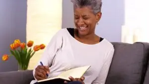 Woman sitting on a couch documenting what is the difference between trauma and complex trauma in a book.
