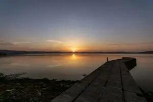 A quiet lake at sunrise with a stony shore and wooden pier extending into the water—evoking stillness, reflection, and emotional depth in the context of disenfranchised grief in Indigenous communities.