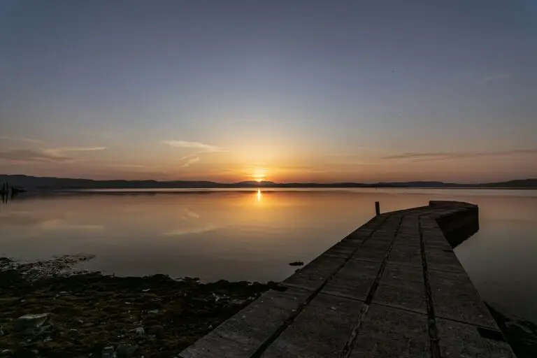A quiet lake at sunrise with a stony shore and wooden pier extending into the water—evoking stillness, reflection, and emotional depth in the context of disenfranchised grief in Indigenous communities.