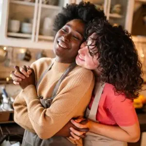 A queer couple embracing in a cozy kitchen, sharing a moment of warmth and connection. The image reflects healing grounded in anti-oppressive, trauma-informed care that honors diverse identities and safe, affirming relationships.