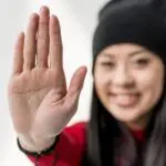 A smiling woman holds up one hand in a gentle stop gesture, expressing confident boundaries. Her expression conveys clarity, assertiveness and self-respect.