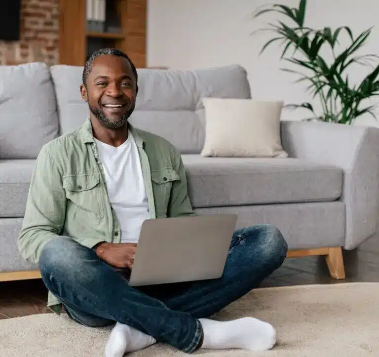 Smiling man having an online trauma-informed coaching session at home with his laptop.