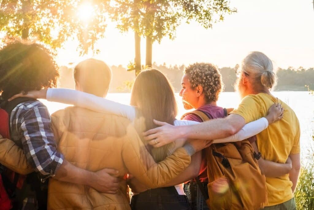 Four friends embracing each other outdoors at sunset, seen from behind — symbolizing connection, support, and trust in relationships after trauma counselling.