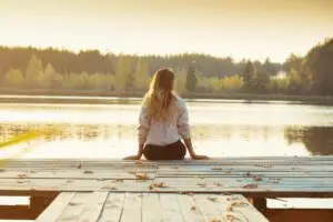 Woman sitting quietly on a wooden pier surrounded by fallen leaves, symbolizing reflection, releasing the past, and healing with EMDR for childhood trauma.