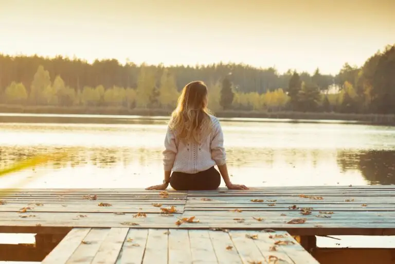 Woman sitting quietly on a wooden pier surrounded by fallen leaves, symbolizing reflection, releasing the past, and healing with EMDR for childhood trauma.