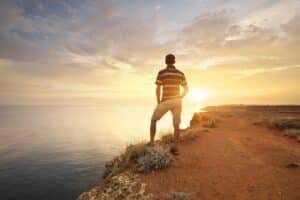 Person standing on a mountaintop at sunset, overlooking a calm sea — symbolizing the strength, clarity, and inner peace found in healing relational trauma.