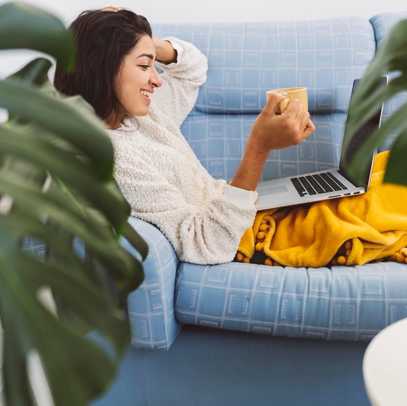 Woman sitting on her sofa with a cup of coffee and a laptop during an online counselling for trauma session.