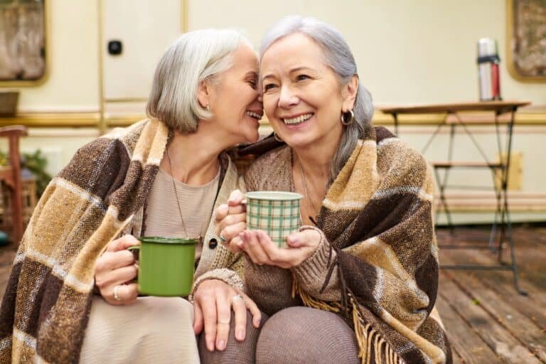 Lesbian couple with coffee and blanket outdoors - healthy boundaries for adults with childhood trauma enable connection.