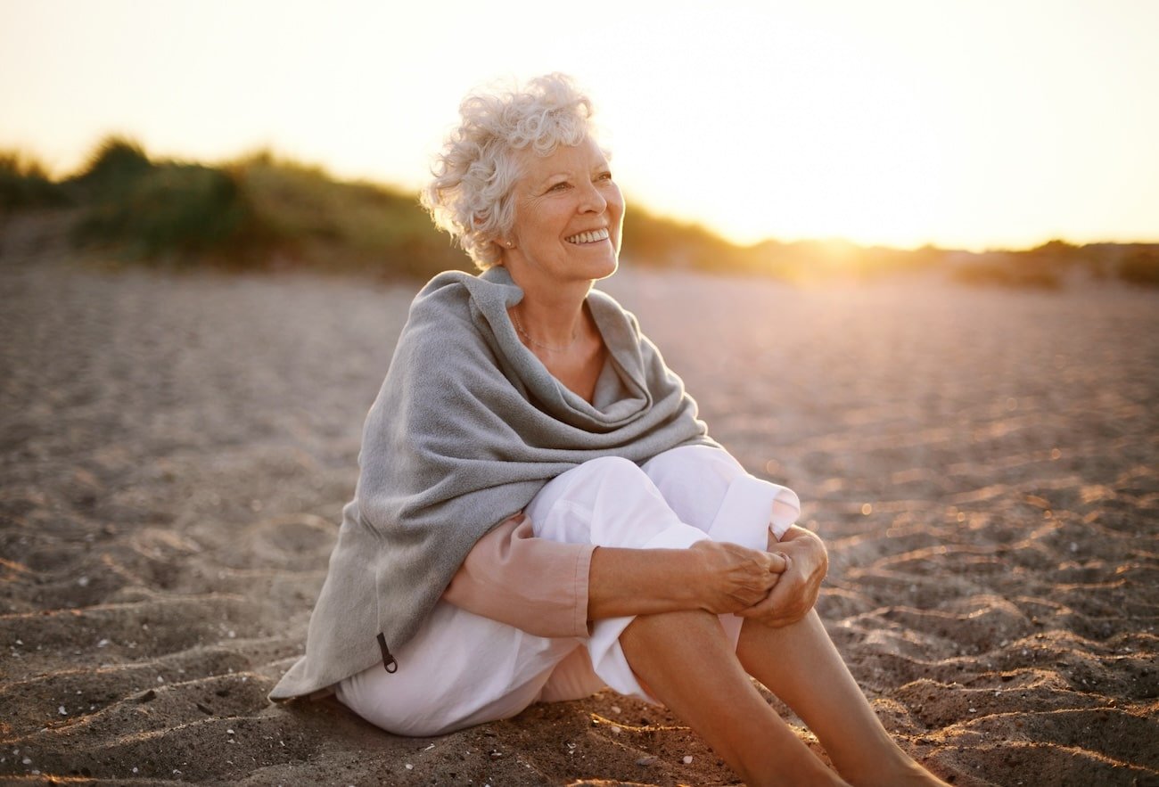 A white woman sitting at the beach during sunset, symbolizing healing with trauma-informed grief counselling online.