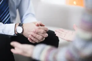 Close-up of a man’s hands resting on his lap during a trauma-informed grief counselling session in a counselling office.